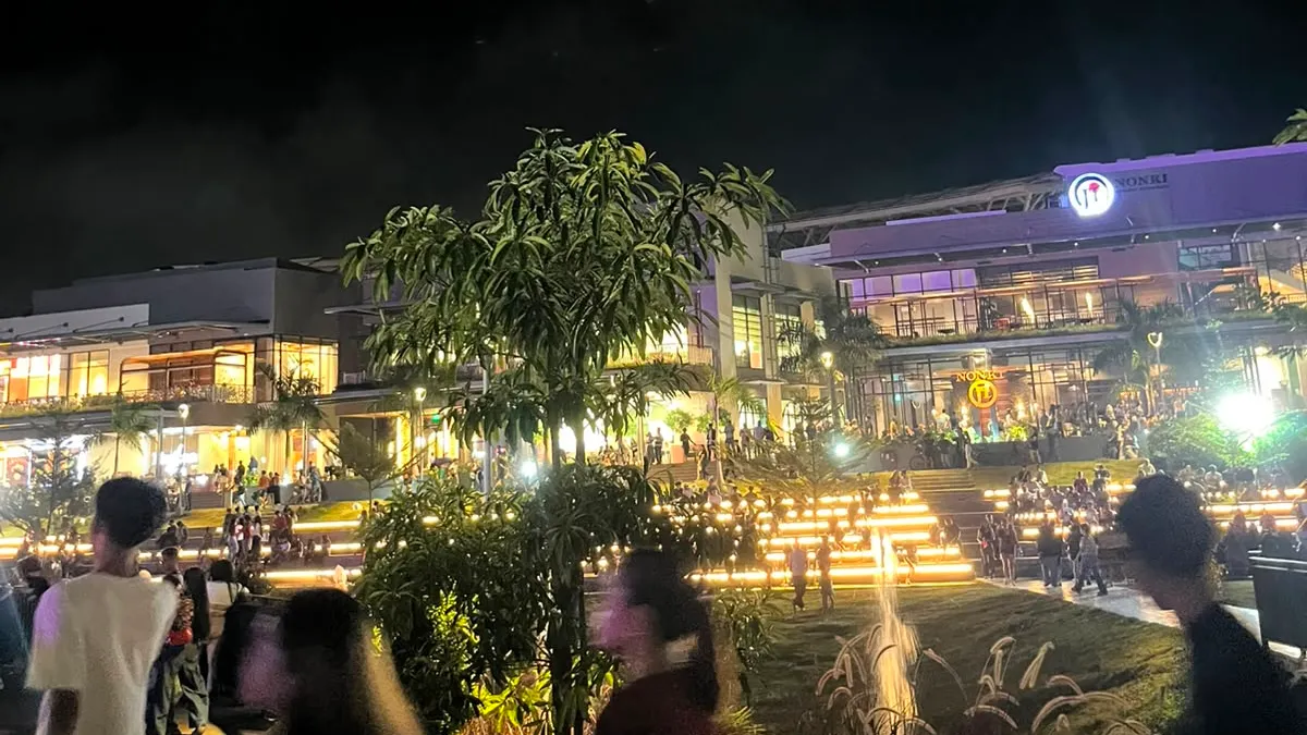 People walking the lawn in front of a lit lifestyle mall at night