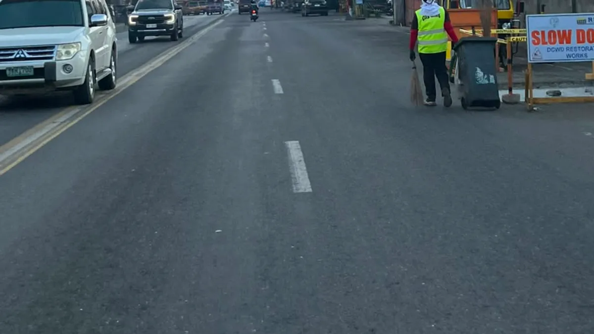 Road works in progress with a hi-vis worker and a slow-down sign on a city road